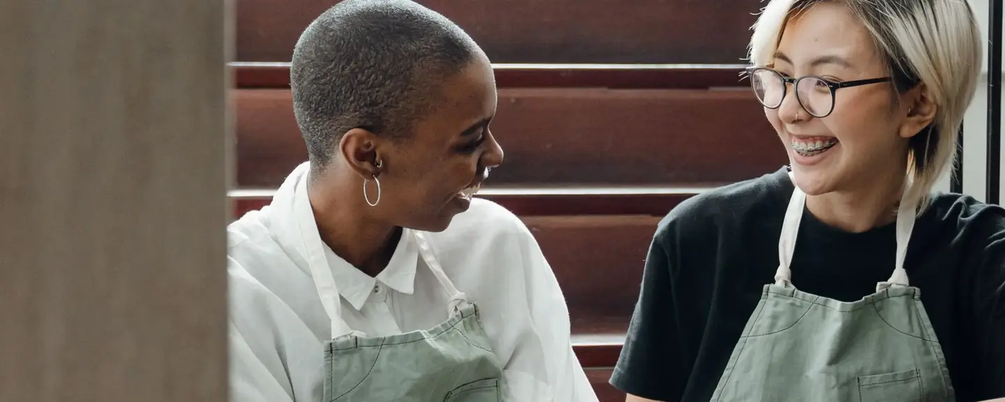 Two servers in aprons laughing together on a café staircase.
