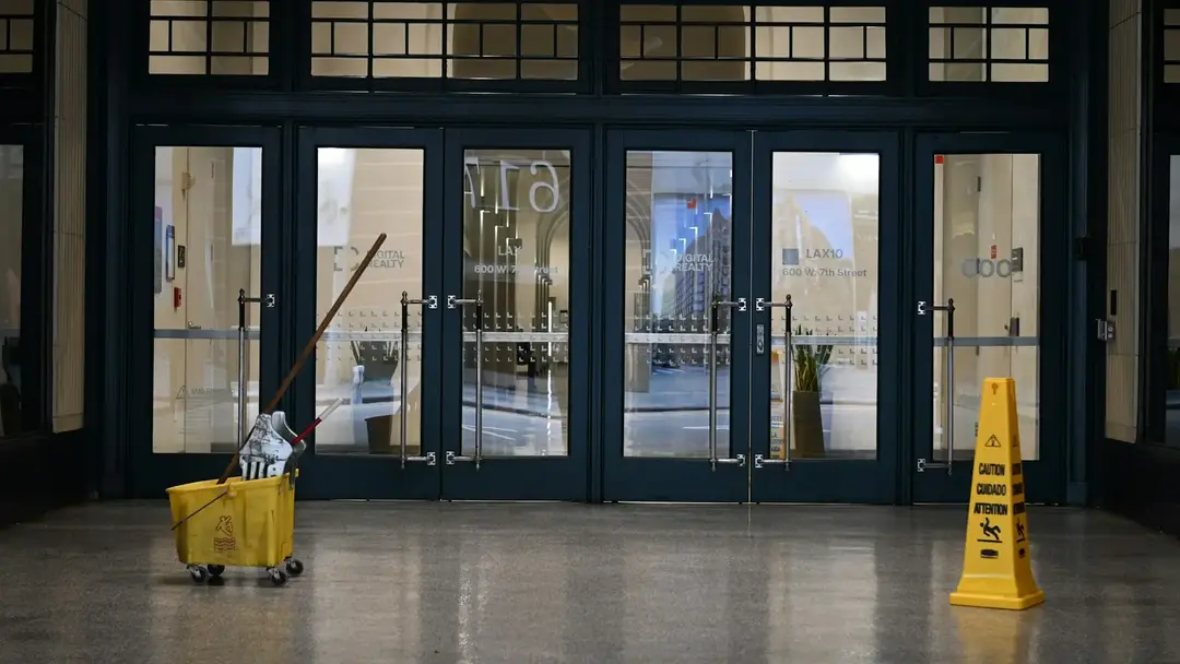 A yellow mop bucket and a wet-floor sign standing alone in a large tiled lobby.