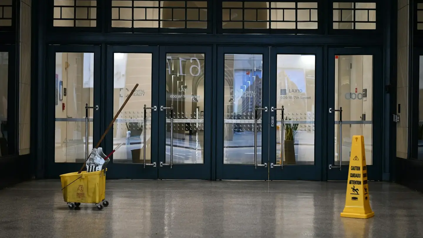 A yellow mop bucket and a wet-floor sign standing alone in a large tiled lobby.
