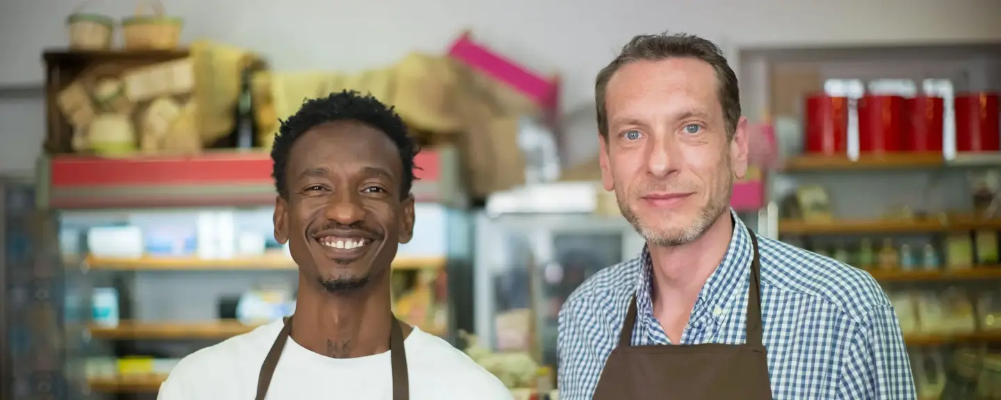 Two shop assistants in aprons smiling in a grocery shop.