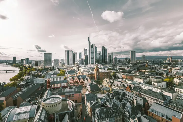 An aerial view of Frankfurt under an overcast sky: the red roofs of the old town in the foreground, the banking towers and the river Main behind.