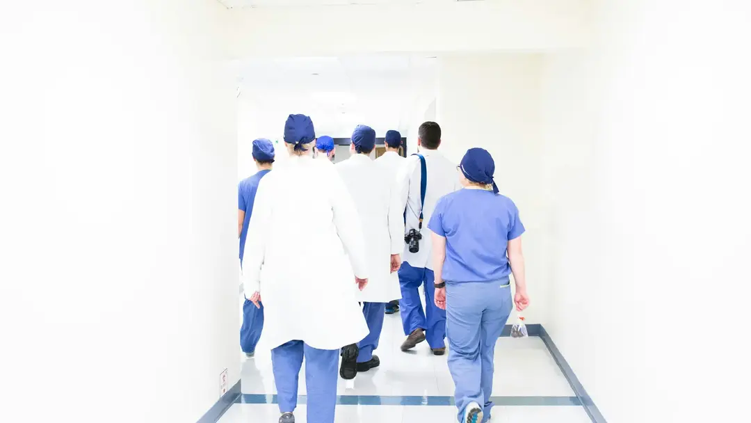 Hospital staff in scrubs and white coats walking away down a bright corridor.