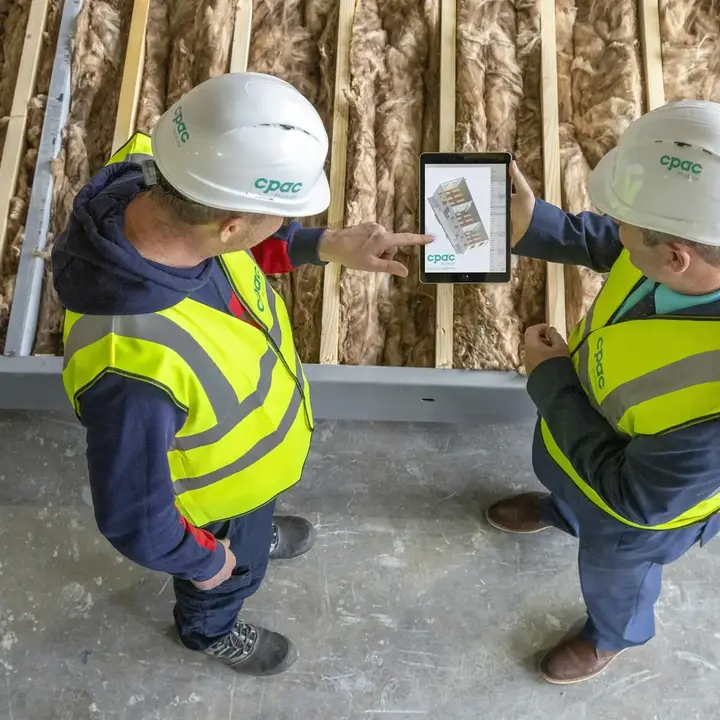 Two workers in hi-vis reading the day’s jobs from a tablet on a building site.