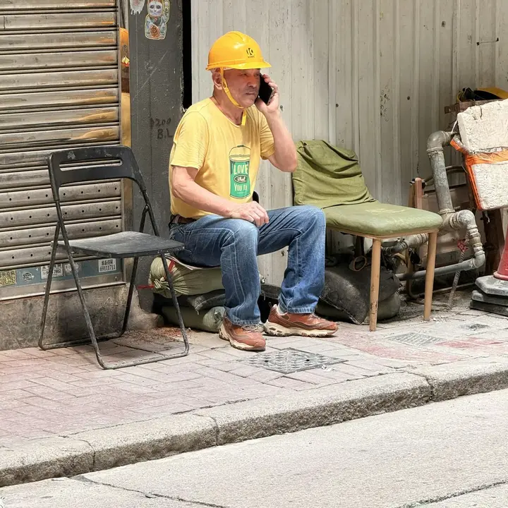 A worker in a hard hat taking a phone call on a break outside a depot.