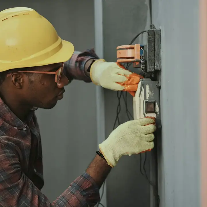 An electrician in a hard hat testing terminals inside an electrical panel.