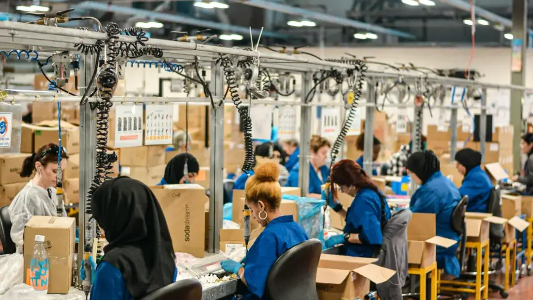 A long assembly line seen down its length, a dozen people in blue workwear at their stations.