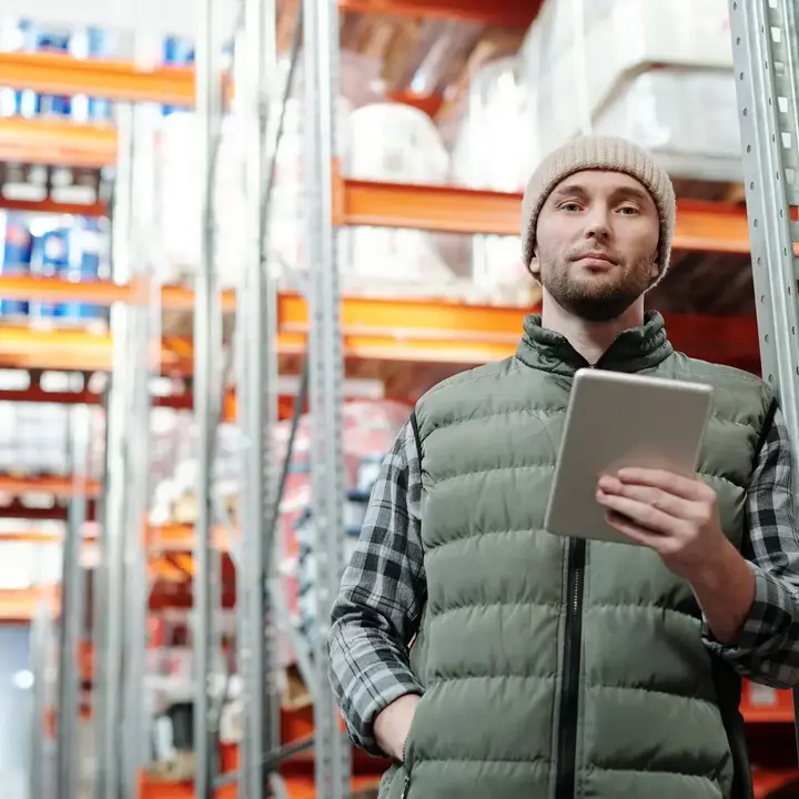 A shift lead standing in a warehouse aisle, holding a tablet.