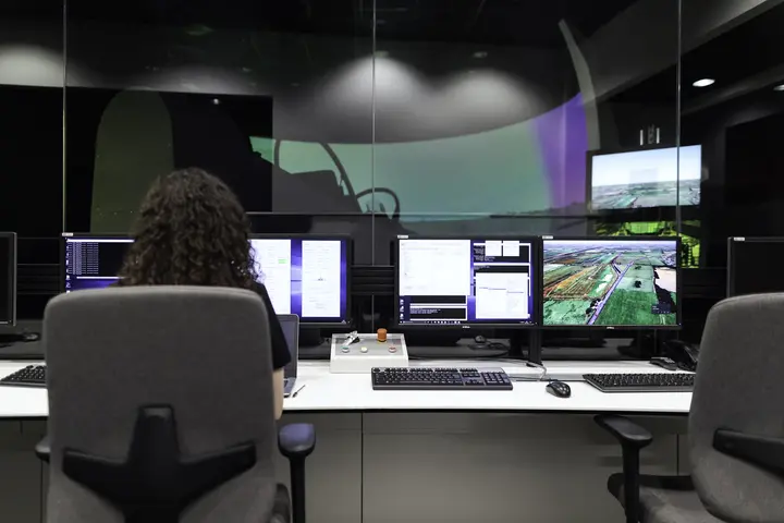 An operations room seen over a shoulder: several screens of live status, one person watching them.