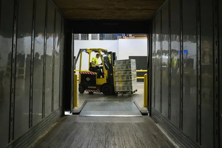 A forklift carrying a pallet up the ramp into a trailer, seen from inside the trailer.