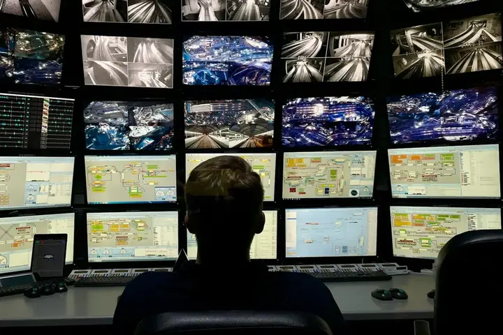 An operator alone at a traffic control desk, facing a wall of camera feeds and schematic displays.