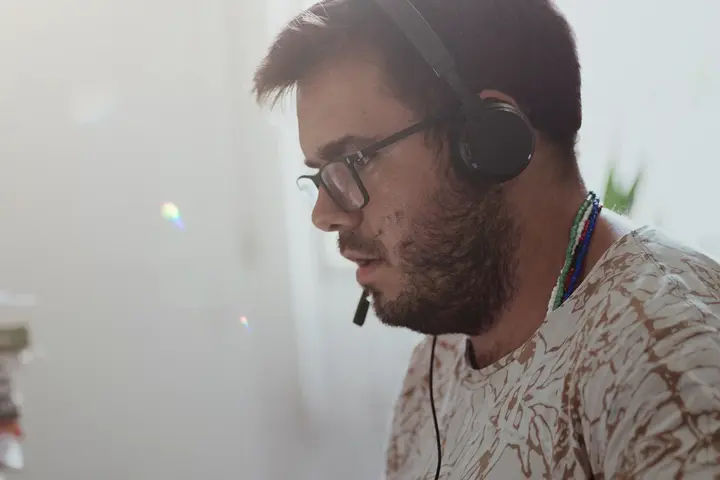 A person in profile wearing a headset, mid-call, with a monitor behind them.